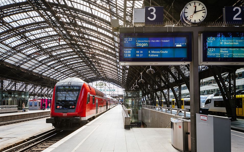 Ein Reisender informiert sich vor einer DB Information per Smartphone zu den Bahnfahrten.
