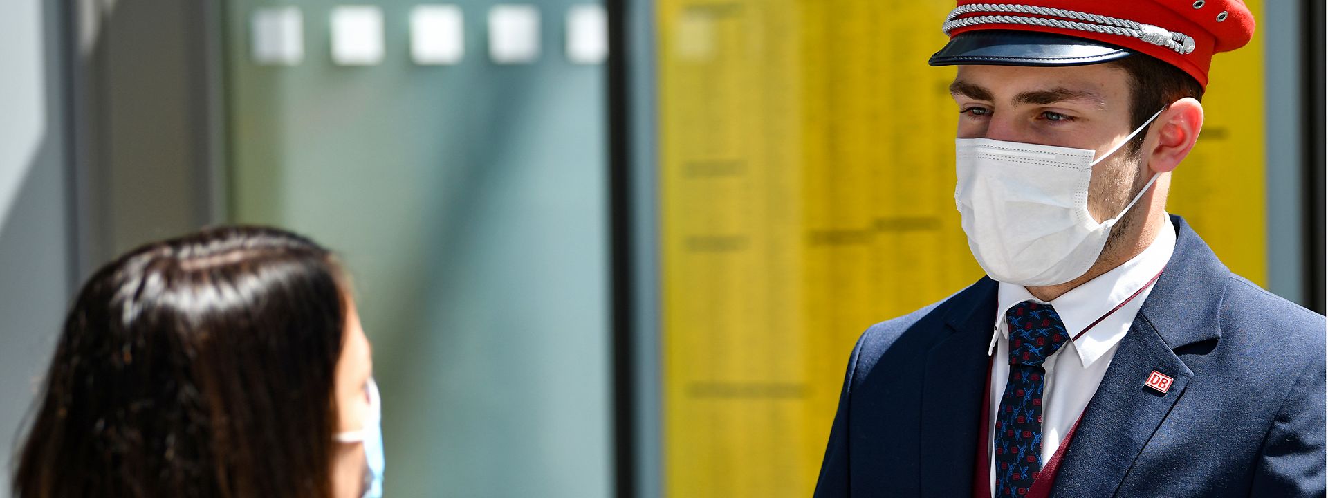 Quelle: DB AG/Oliver Lang Ein junger Servicemitarbeiter der Deutschen Bahn mit Mund-Nasen-Schutz im Gespräch mit einer Reisenden
