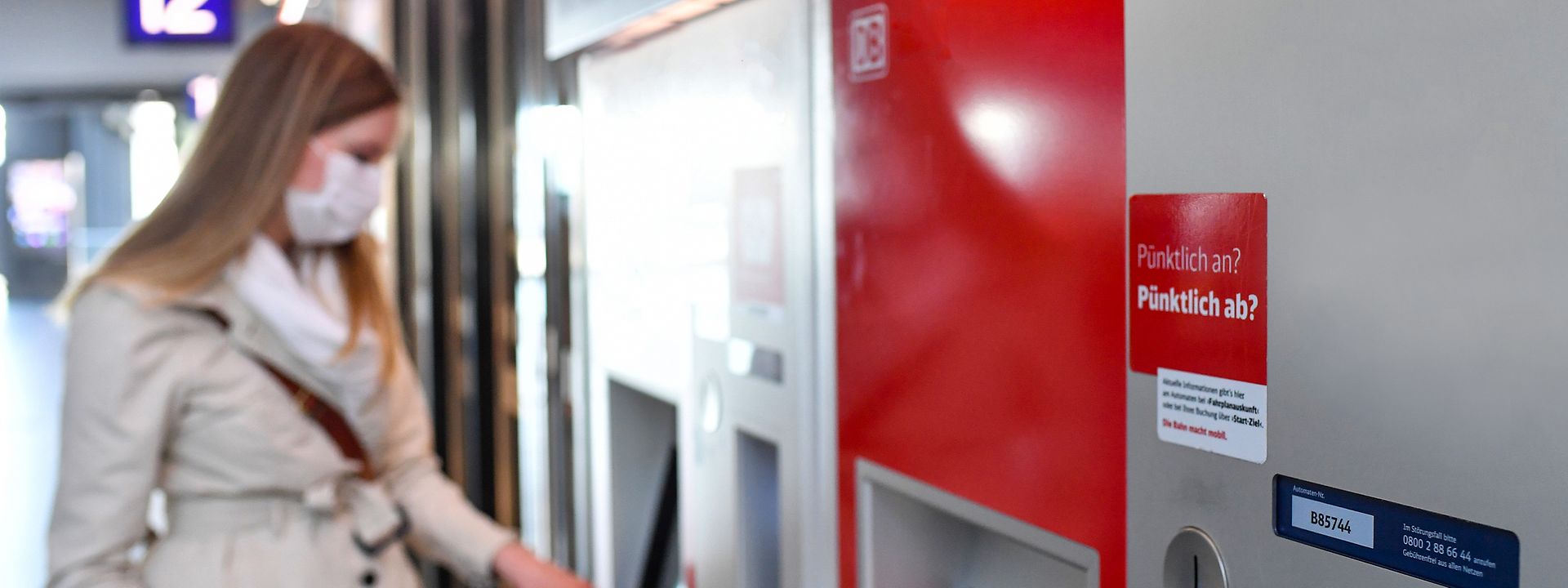 Quelle: DB AG/Oliver Lang Eine Frau mit Mund-Nasen-Schutz steht an einem Fahrkartenautomaten und löst ein Fahrticket.