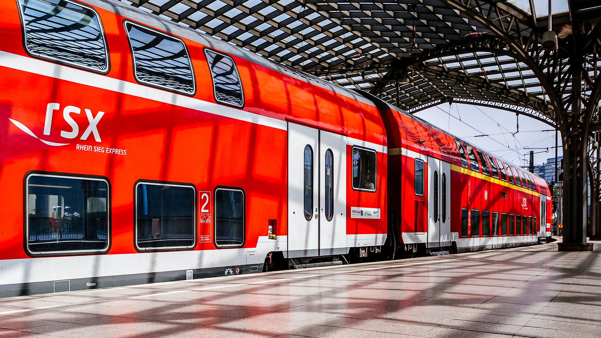 Roter RSX-Doppelstockwagen an einem Gleis in einem überdachten Bahnhof, das RSX-Logo ist an der Seite gut sichtbar