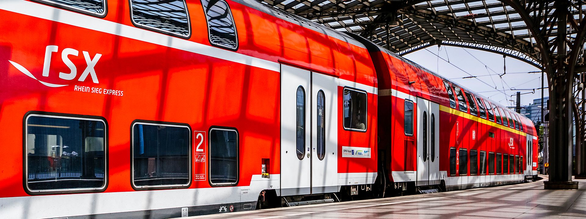 Roter RSX-Doppelstockwagen an einem Gleis in einem überdachten Bahnhof, das RSX-Logo ist an der Seite gut sichtbar
