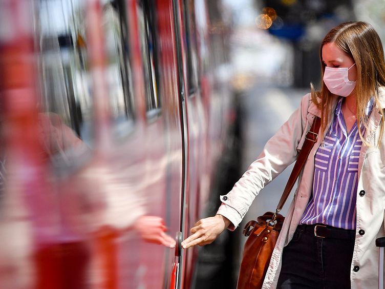 Eine Reisende mit Mund-Nasen-Schutz am Gleis eines Bahnhofs bedient die Türöffner-Taste eines Regionalzugs.