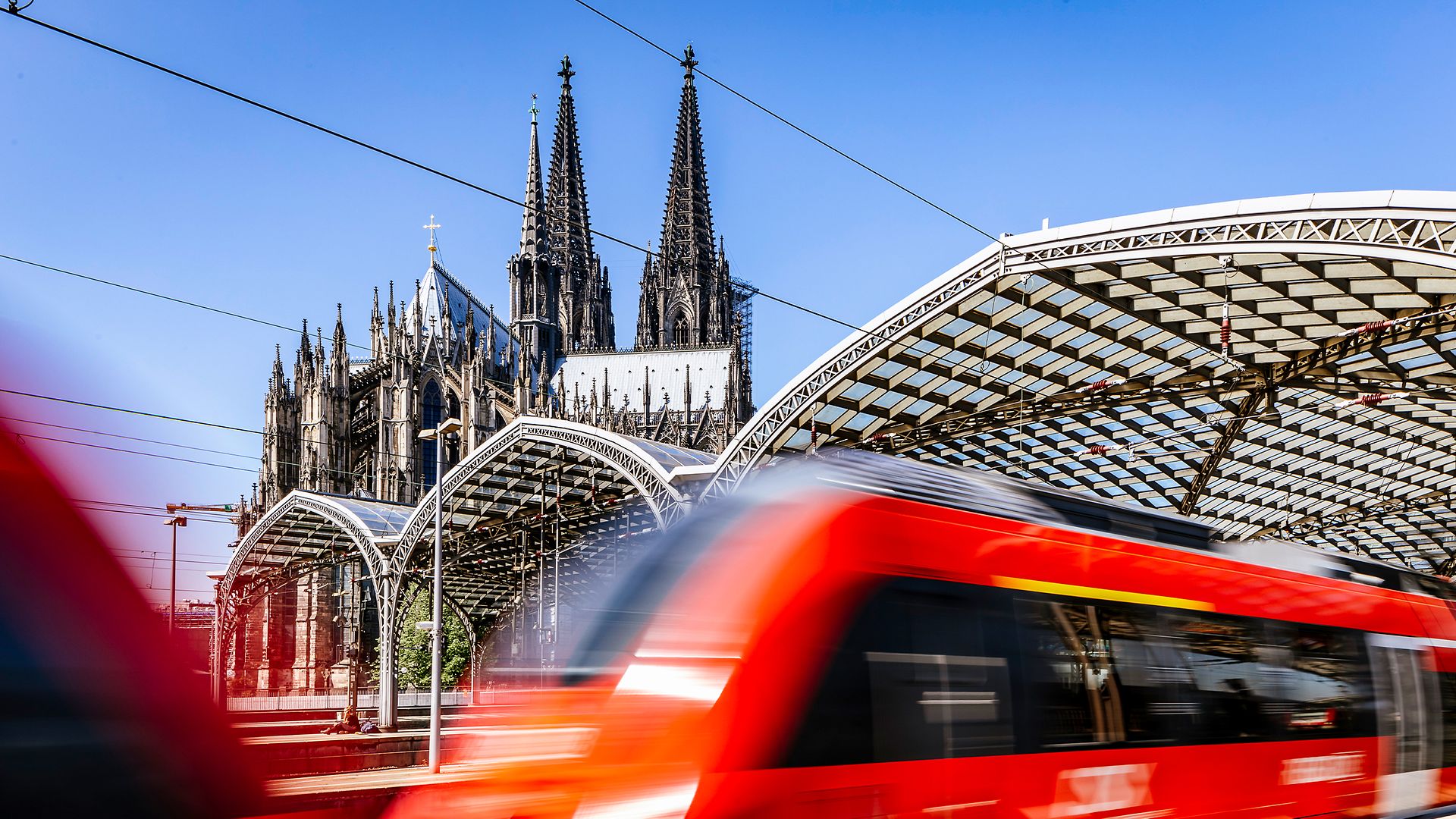 Dynamisches Bild eines vom Bahnhof ausfahrenden Zugs mit Kölner Dom im Hintergrund.