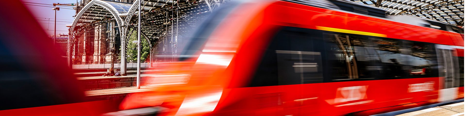 Dynamisches Bild eines vom Bahnhof ausfahrenden Zugs mit Kölner Dom im Hintergrund.
