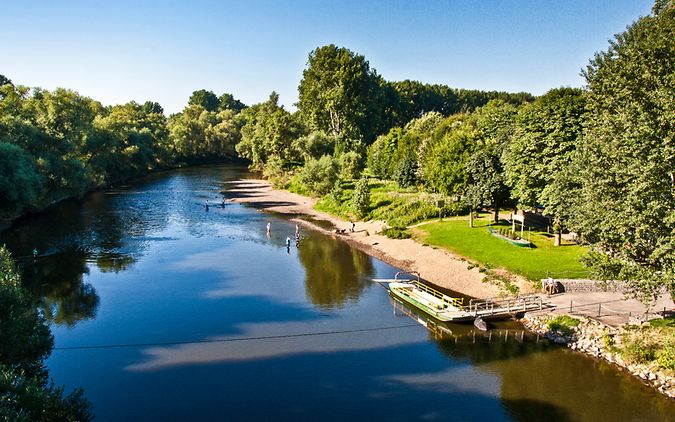 Eine Fähre inmitten von grüner Natur mit badenden Personen im Fluss.