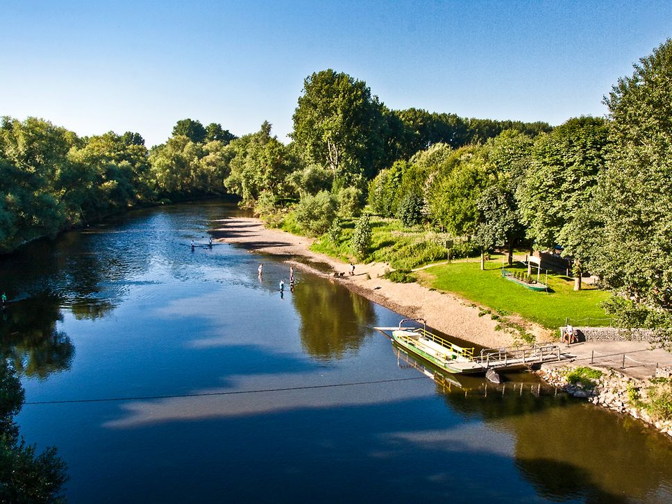 Eine Fähre inmitten von grüner Natur mit badenden Personen im Fluss.